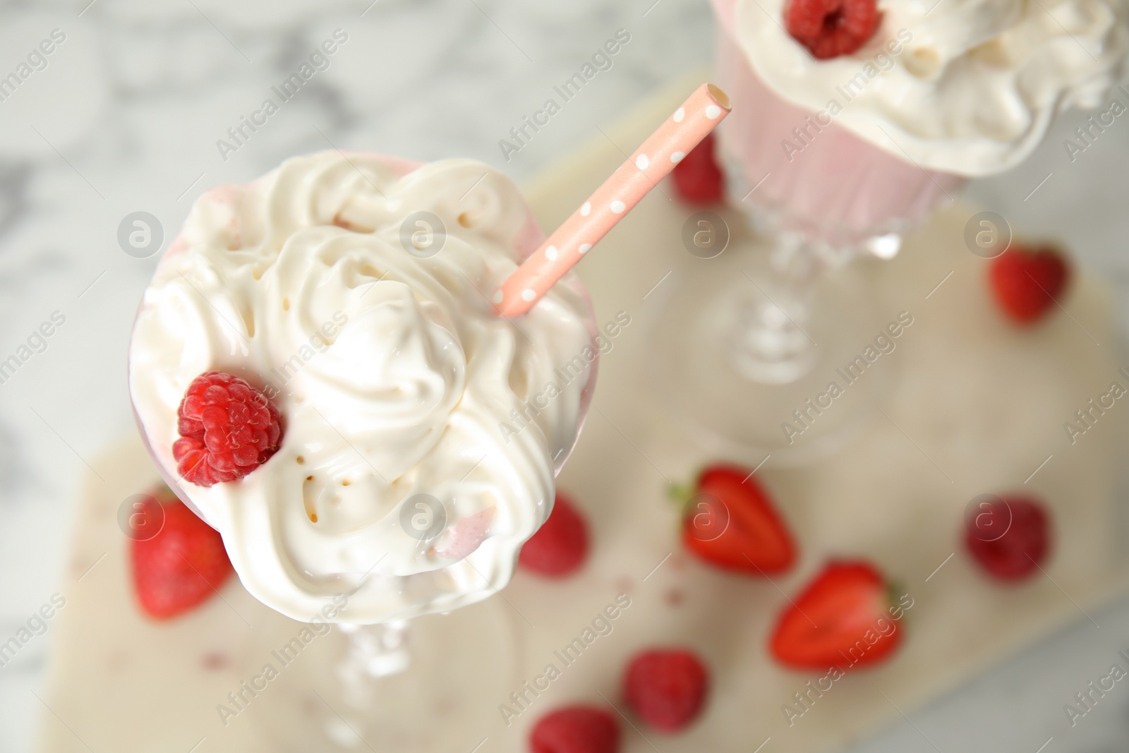 Photo of Tasty milk shake with whipped cream and fresh berries on light table, closeup