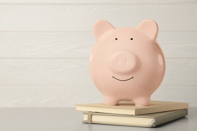 Ceramic piggy bank and notebooks on light grey table. Space for text