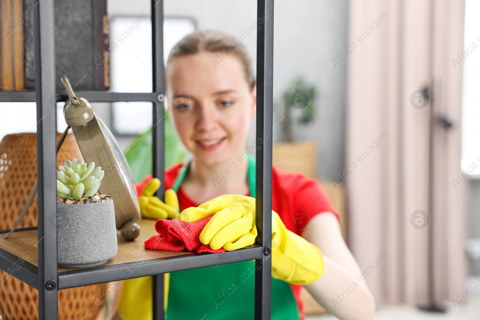 Photo of Woman cleaning shelving unit with rag at home, selective focus