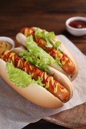 Photo of Tasty hot dogs with lettuce, ketchup and mustard on board