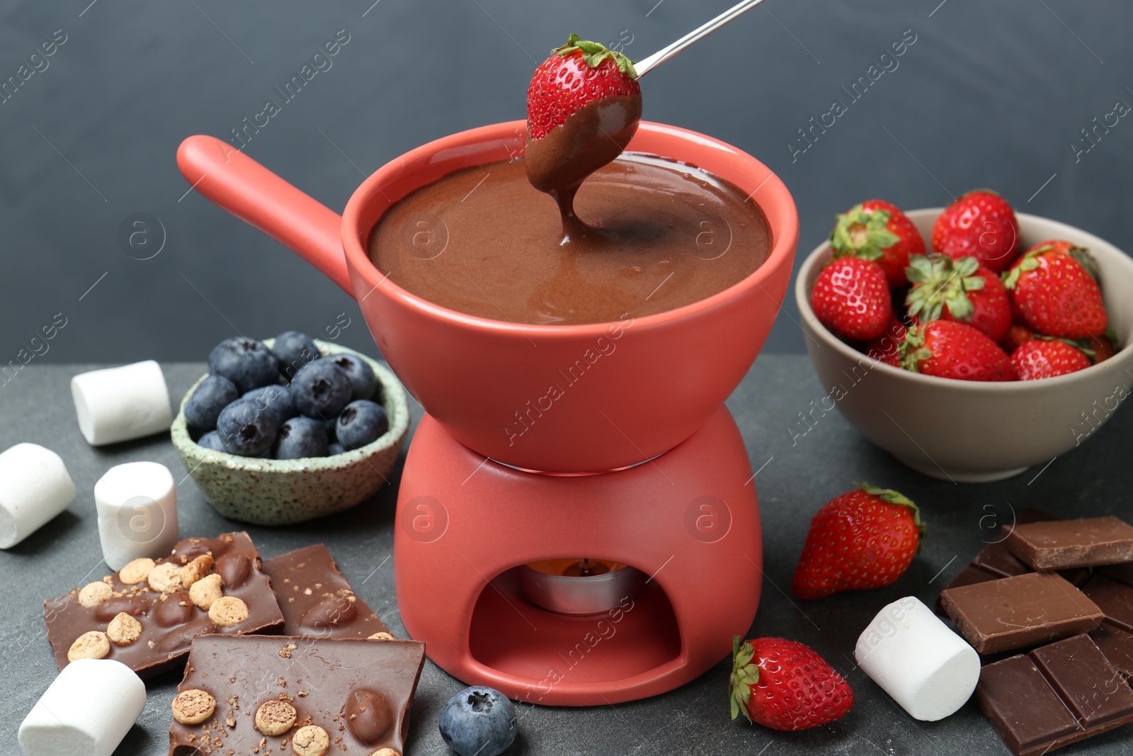 Photo of Dipping fresh strawberry in fondue pot with melted chocolate at grey table