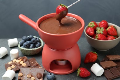 Photo of Dipping fresh strawberry in fondue pot with melted chocolate at grey table
