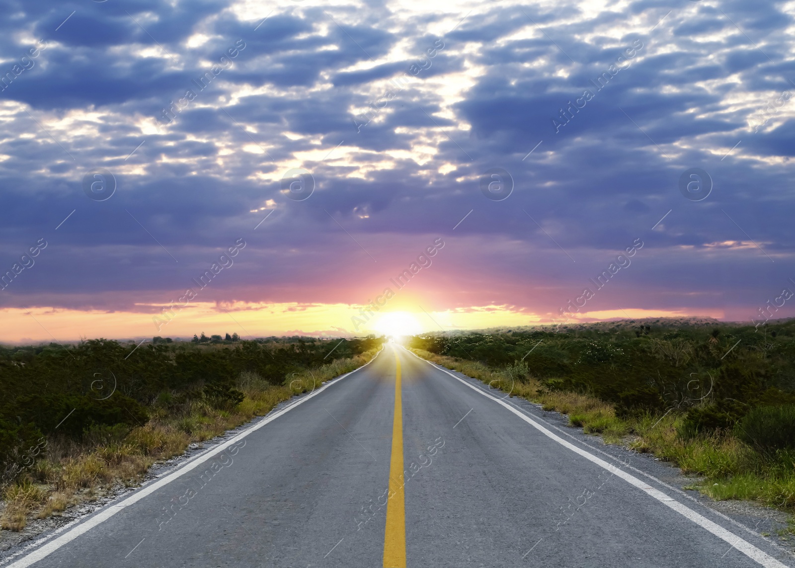 Image of Empty asphalt road through field at sunset