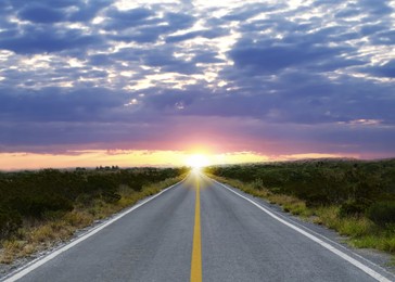 Empty asphalt road through field at sunset