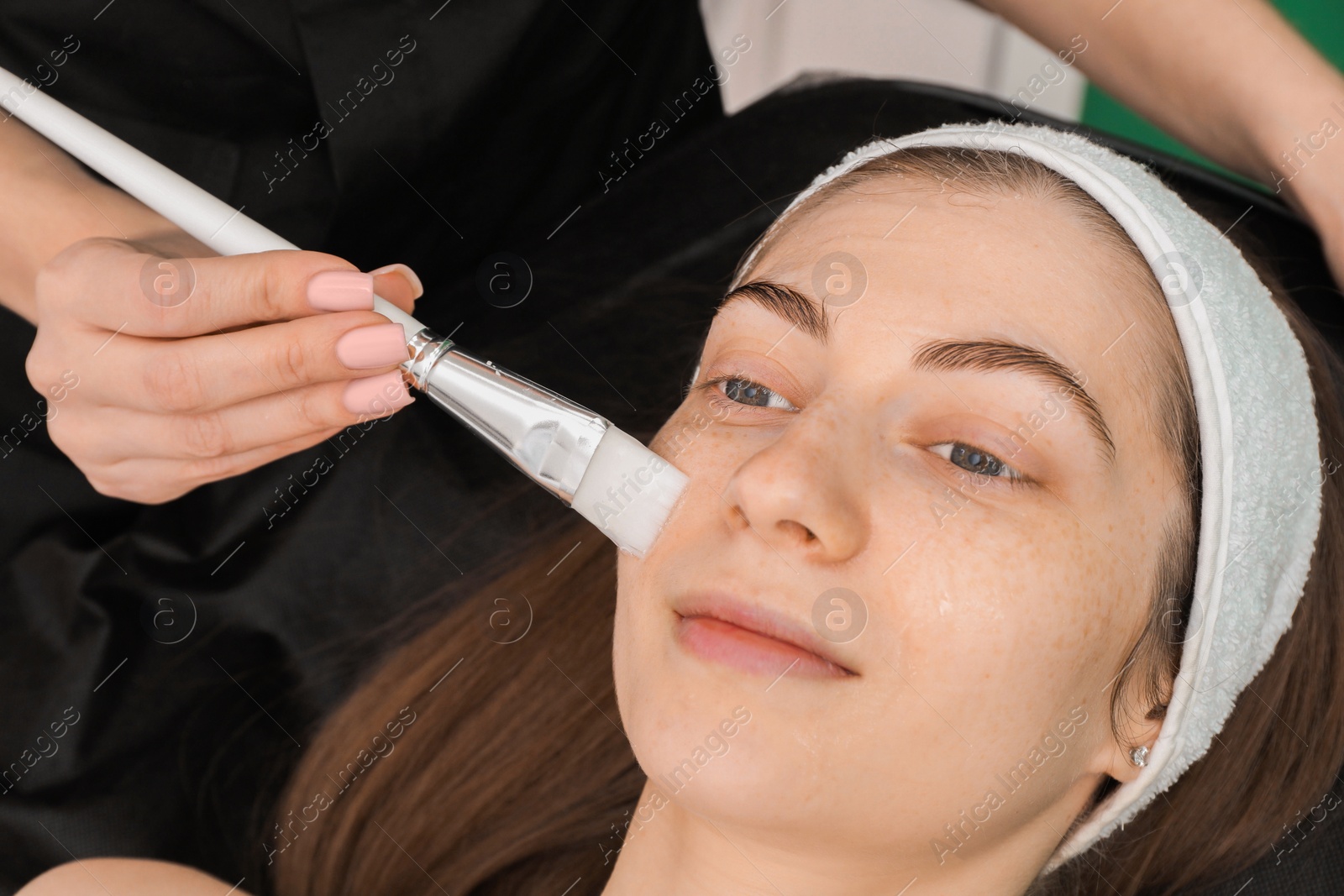 Photo of Cosmetologist applying mask on woman's face indoors, closeup