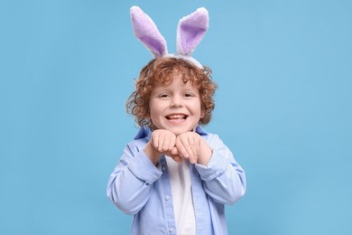 Photo of Portrait of happy boy wearing bunny ears headband on light blue background. Easter celebration