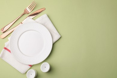 Photo of Clean plate with cutlery and napkin on light green background, flat lay. Space for text