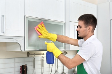 Photo of Male janitor cleaning kitchen furniture with rag in house