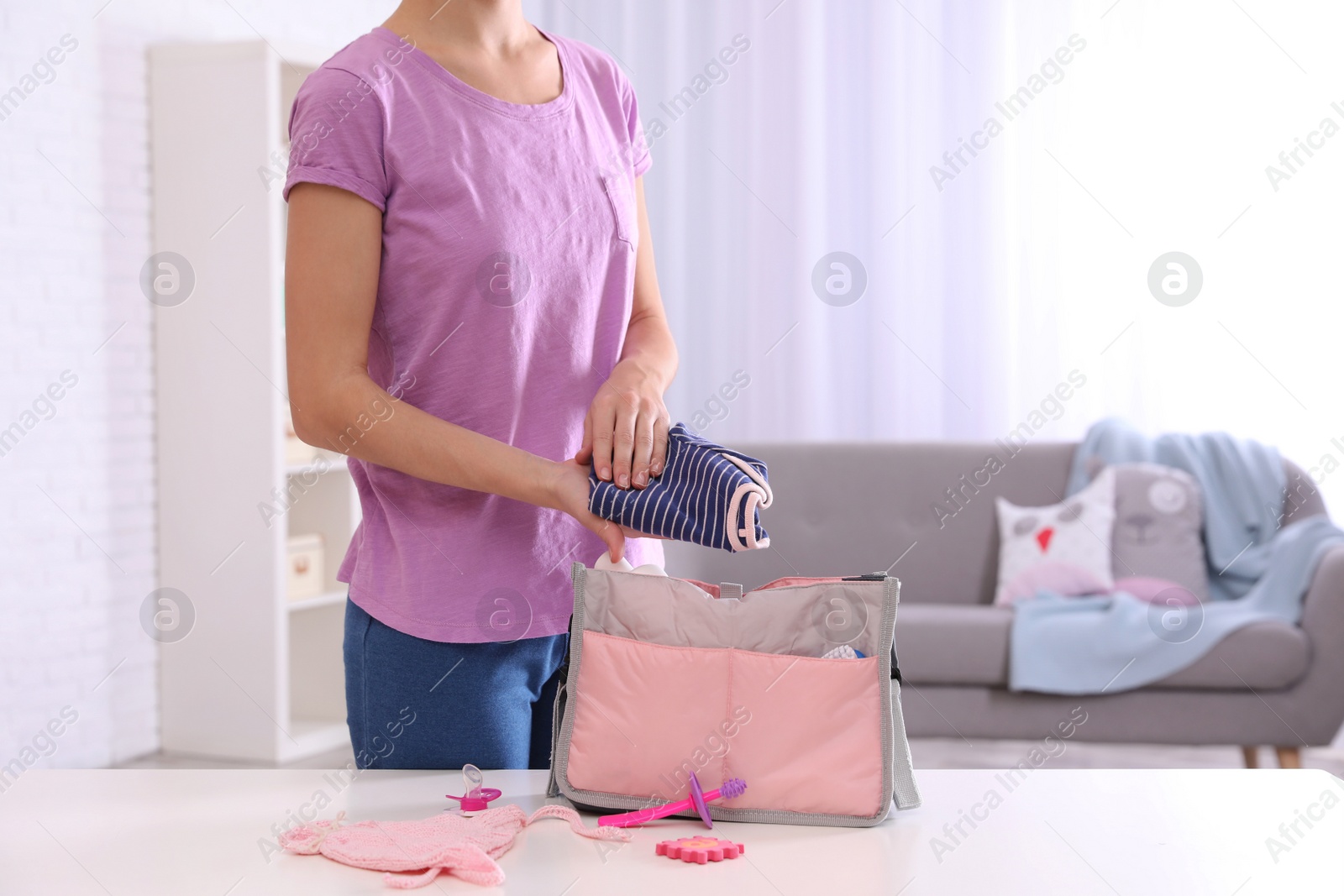 Photo of Woman packing baby accessories into maternity bag on table indoors, closeup