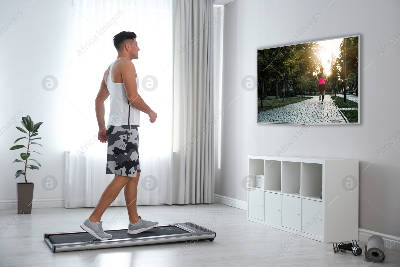 Image of Sporty man training on walking treadmill and watching TV at home