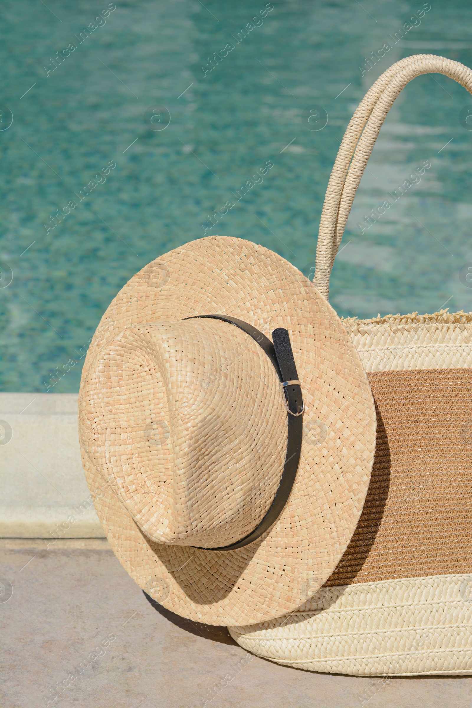 Photo of Stylish bag and hat near outdoor swimming pool on sunny day. Beach accessories