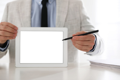 Photo of Businessman holding modern tablet with blank screen at white table in office, closeup