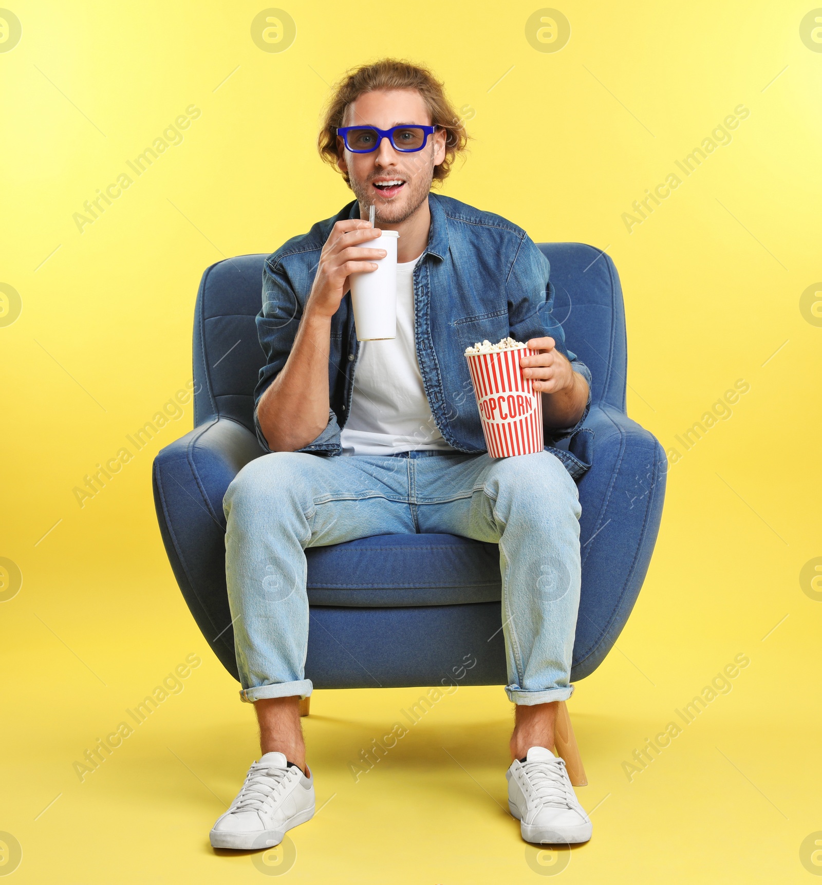 Photo of Emotional man with 3D glasses, popcorn and beverage sitting in armchair during cinema show on color background