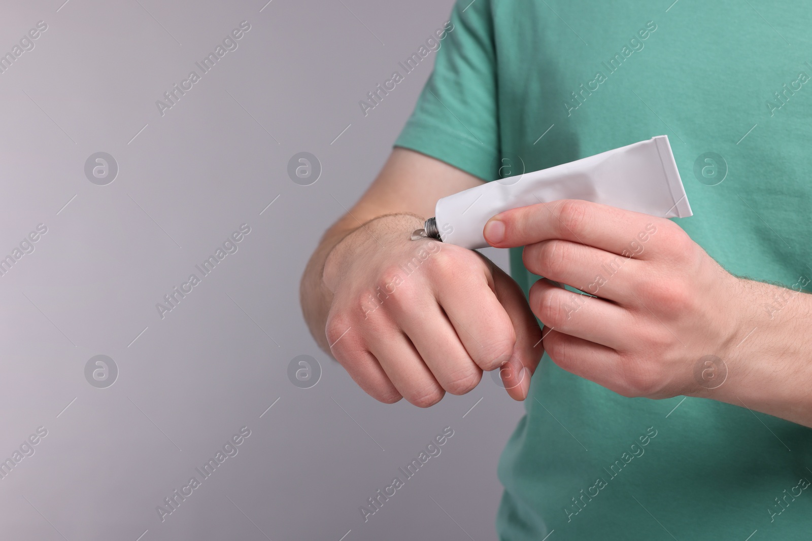 Photo of Man applying ointment from tube onto hand on light grey background, closeup. Space for text