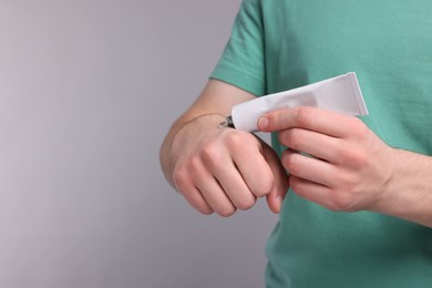 Man applying ointment from tube onto hand on light grey background, closeup. Space for text