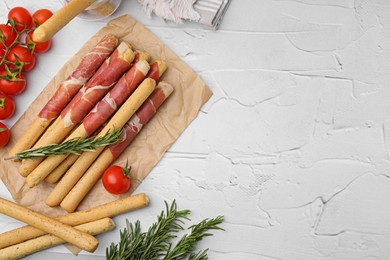 Photo of Delicious grissini sticks with prosciutto and snacks on white table, flat lay. Space for text