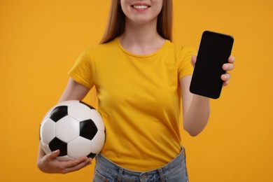 Sports fan with ball and smartphone on yellow background, closeup