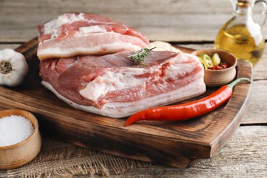 Pieces of raw pork belly, chili pepper, oil, garlic and rosemary on wooden table