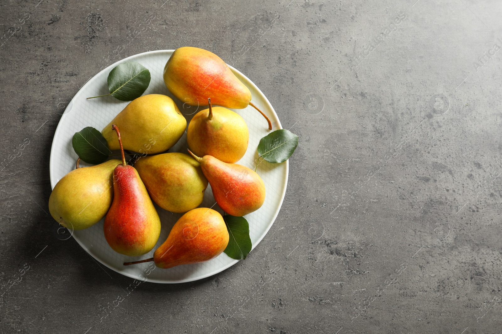 Photo of Plate with ripe pears on grey background, top view. Space for text