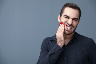 Image of Young man suffering from toothache on grey background, space for text