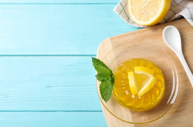 Delicious yellow jelly with lemon slices and mint on light blue wooden table, flat lay. Space for text