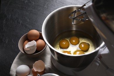 Photo of Making dough. Raw eggs in bowl of stand mixer and ingredients on black table, closeup