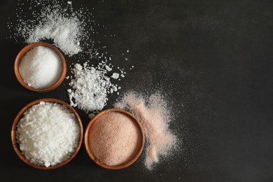 Photo of Different types of organic salt in bowls on black table, flat lay. Space for text