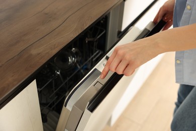 Woman pushing button on dishwasher's door indoors, closeup