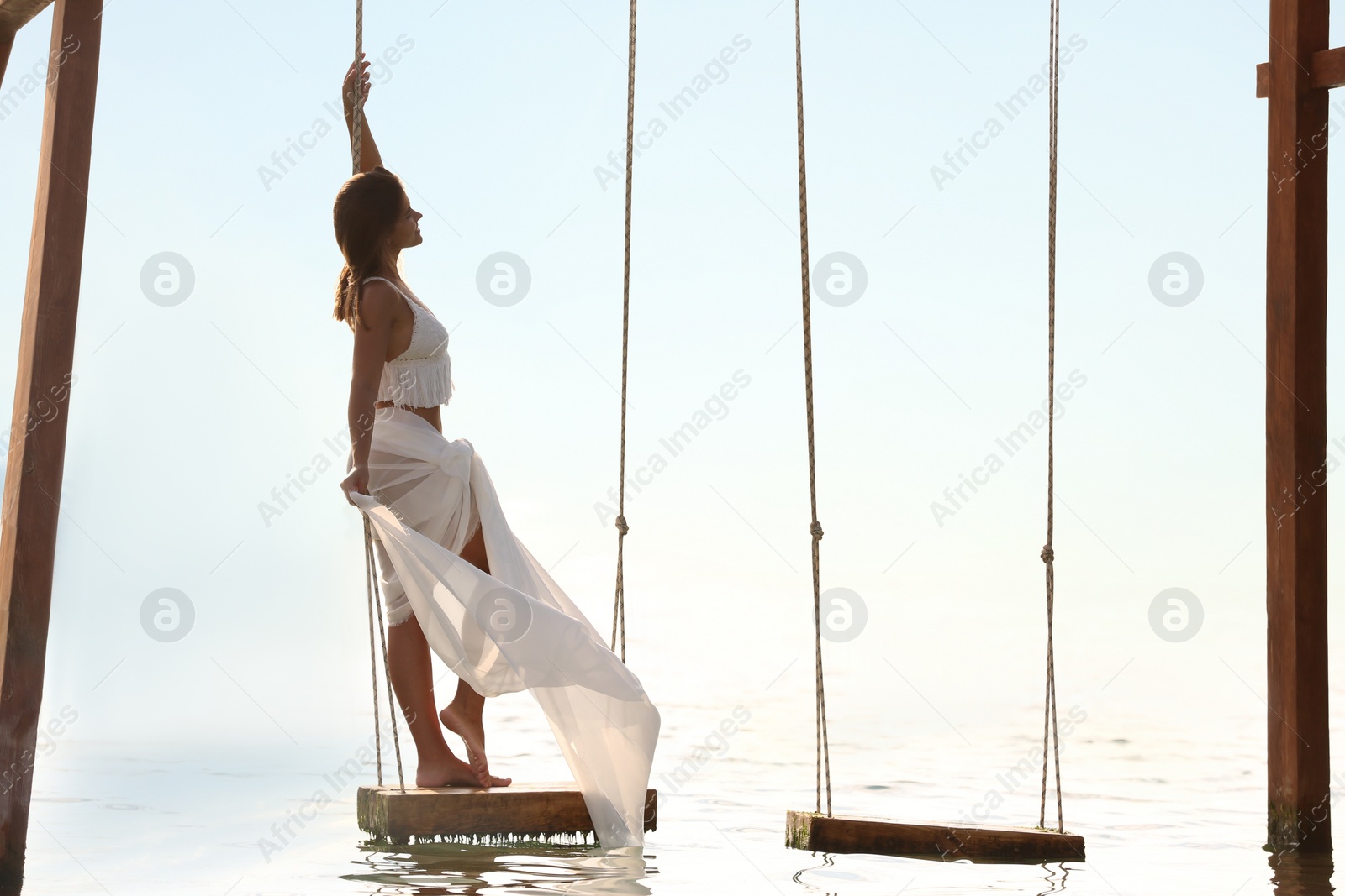 Photo of Young woman enjoying sunrise on swing over water