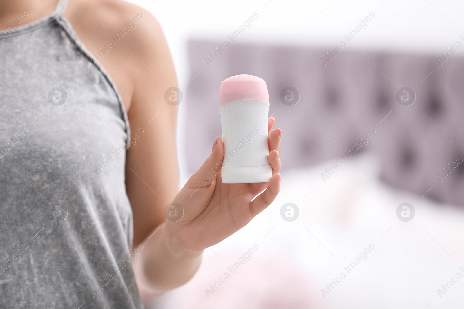 Photo of Beautiful young woman holding deodorant in bedroom, closeup. Space for text