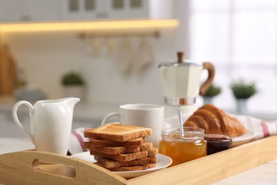 Photo of Breakfast served in kitchen. Tray with toasts, honey, jam, fresh croissant, coffee and pitcher of milk on white table, closeup