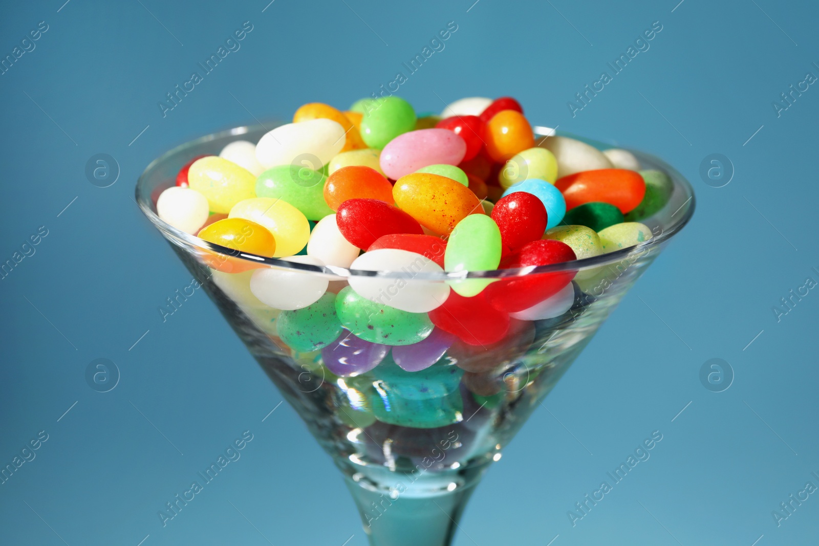 Photo of Beautiful martini glass with colorful candies on light blue background, closeup