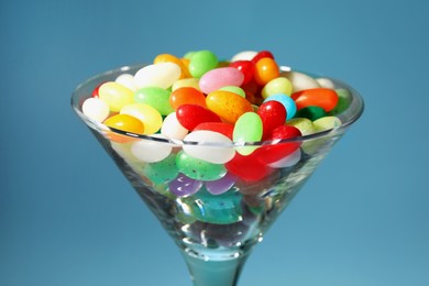 Beautiful martini glass with colorful candies on light blue background, closeup