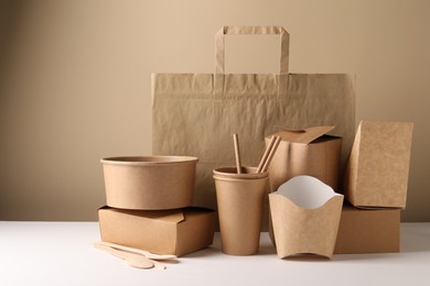 Photo of Eco friendly food packaging. Paper containers, tableware and bag on white table against beige background