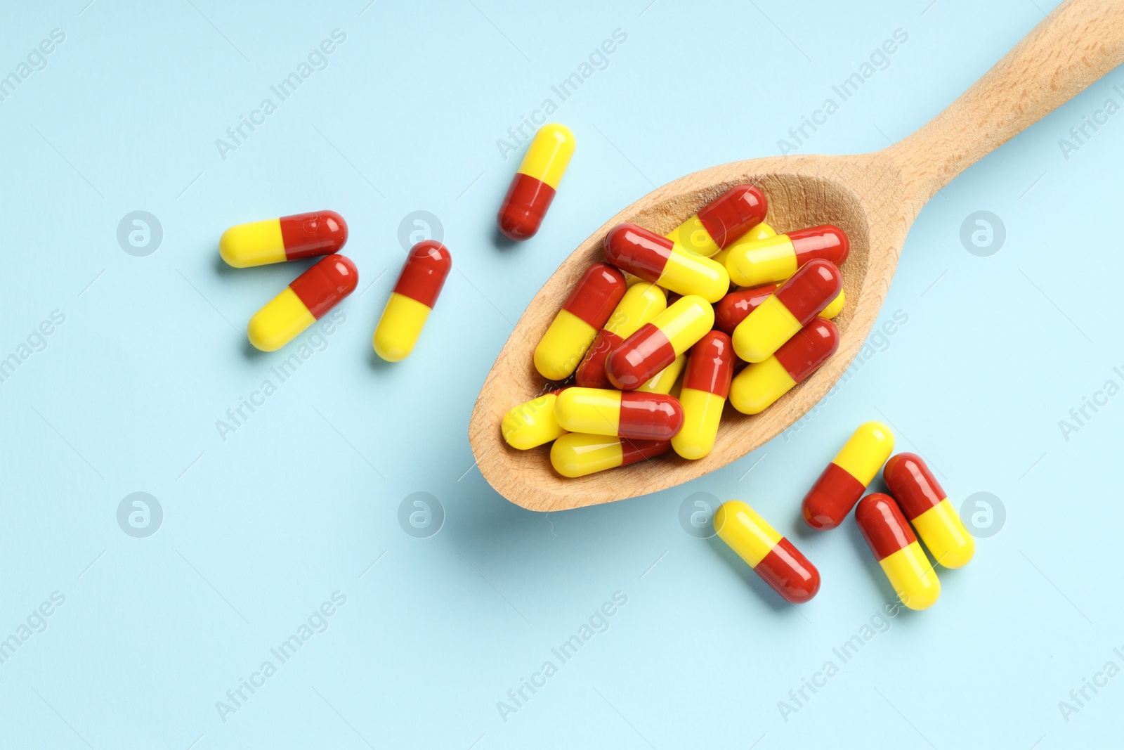 Photo of Antibiotic pills and spoon on light blue background, top view