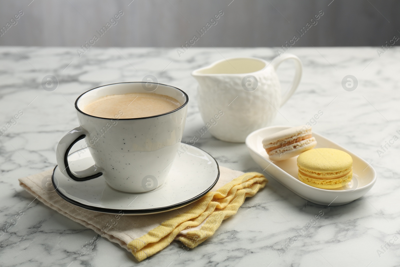 Photo of Tasty cappuccino in cup, macarons, pitcher and saucer on white marble table