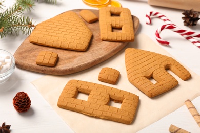 Parts of gingerbread house and ingredients on white table