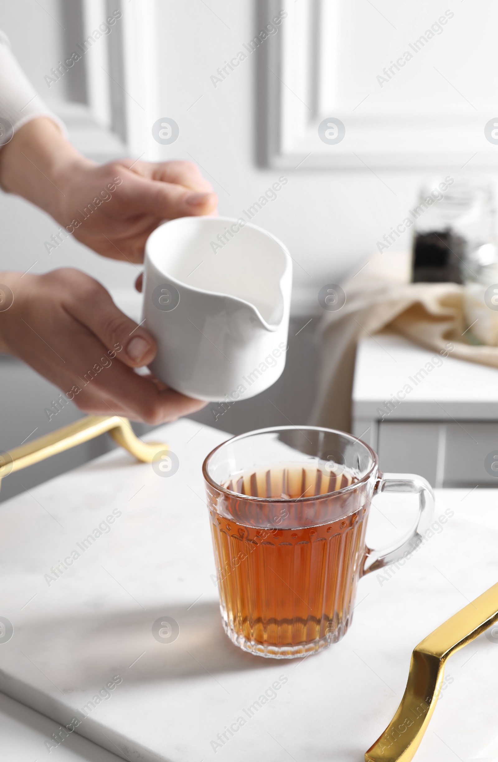 Photo of Woman pouring milk into cup of tea at white table, closeup