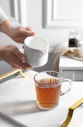 Photo of Woman pouring milk into cup of tea at white table, closeup