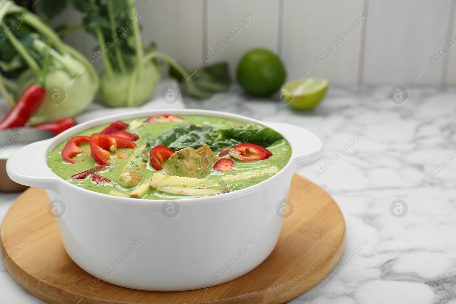 Photo of Saucepan with delicious green curry chicken soup on white marble table