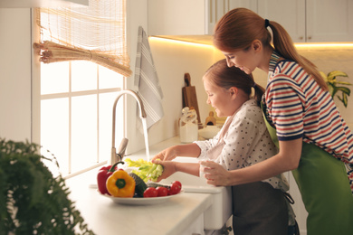 Photo of Mother and daughter washing vegetables in kitchen