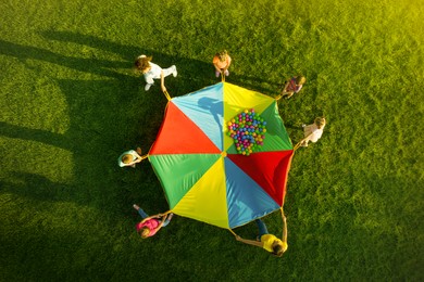 Group of children and teachers playing with rainbow playground parachute on green grass, top view. Summer camp activity