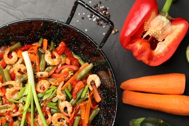 Shrimp stir fry with vegetables in wok and ingredients on black table, flat lay