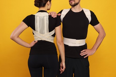Closeup view of man and woman with orthopedic corsets on orange background