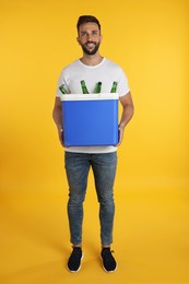 Photo of Happy man holding cool box with bottles of beer on yellow background
