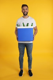 Happy man holding cool box with bottles of beer on yellow background