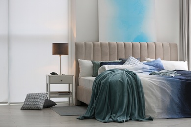 Comfortable bed with pillows and soft blanket in room. Stylish interior design