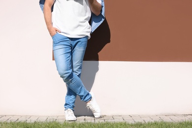 Young hipster man in stylish jeans posing near color wall