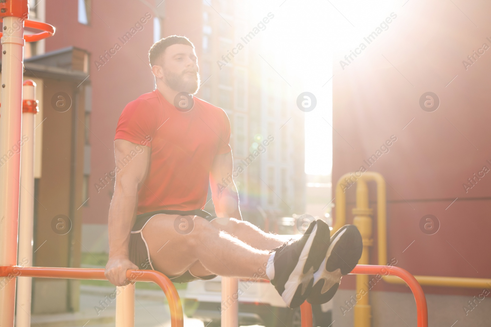 Photo of Man training on parallel bars at outdoor gym on sunny day