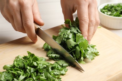 Photo of Woman cutting fresh green cilantro at table, closeup